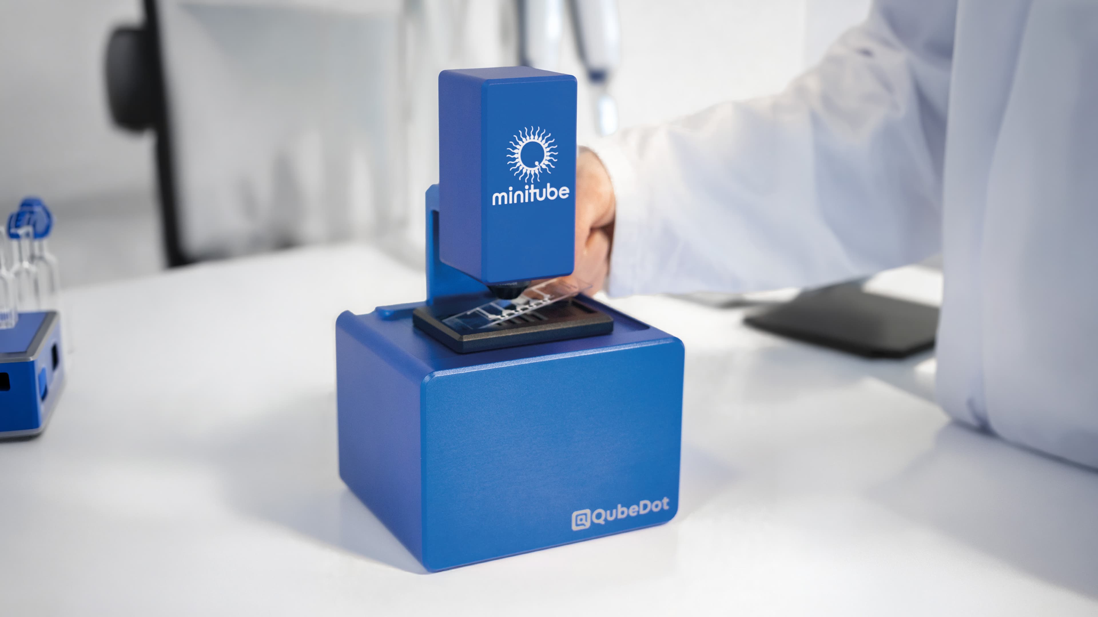 A laboratory technician placing a chamber slide into the blue MiniQube digital microscope by Minitube for analysis.